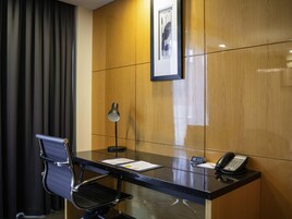 A hotel room with a desk, chair, telephone, and a framed picture on the wall.
