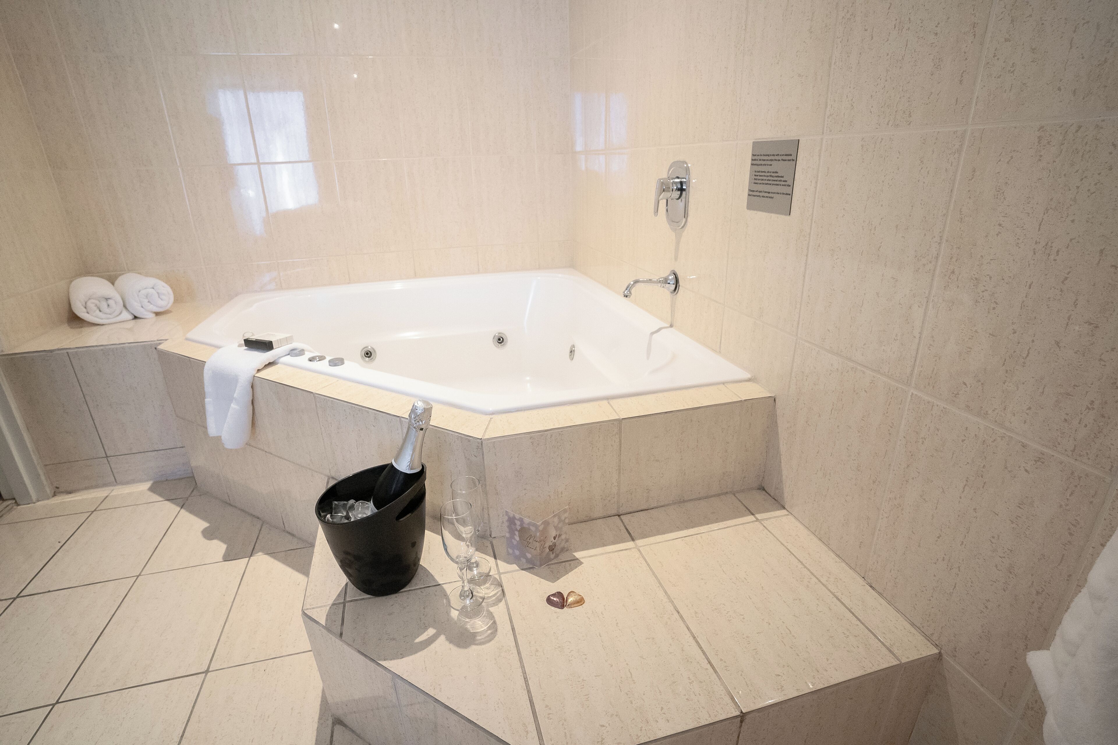 Un baño moderno con una bañera grande, un perchero con toallas, una botella de champán y un cesto de basura.