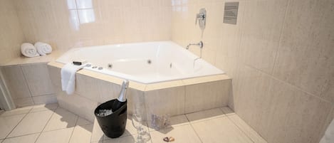 Un baño moderno con una bañera grande, un perchero con toallas, una botella de champán y un cesto de basura.