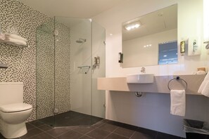 Un baño moderno con ducha envuelta en vidrio, inodoro, lavabo y espejo.