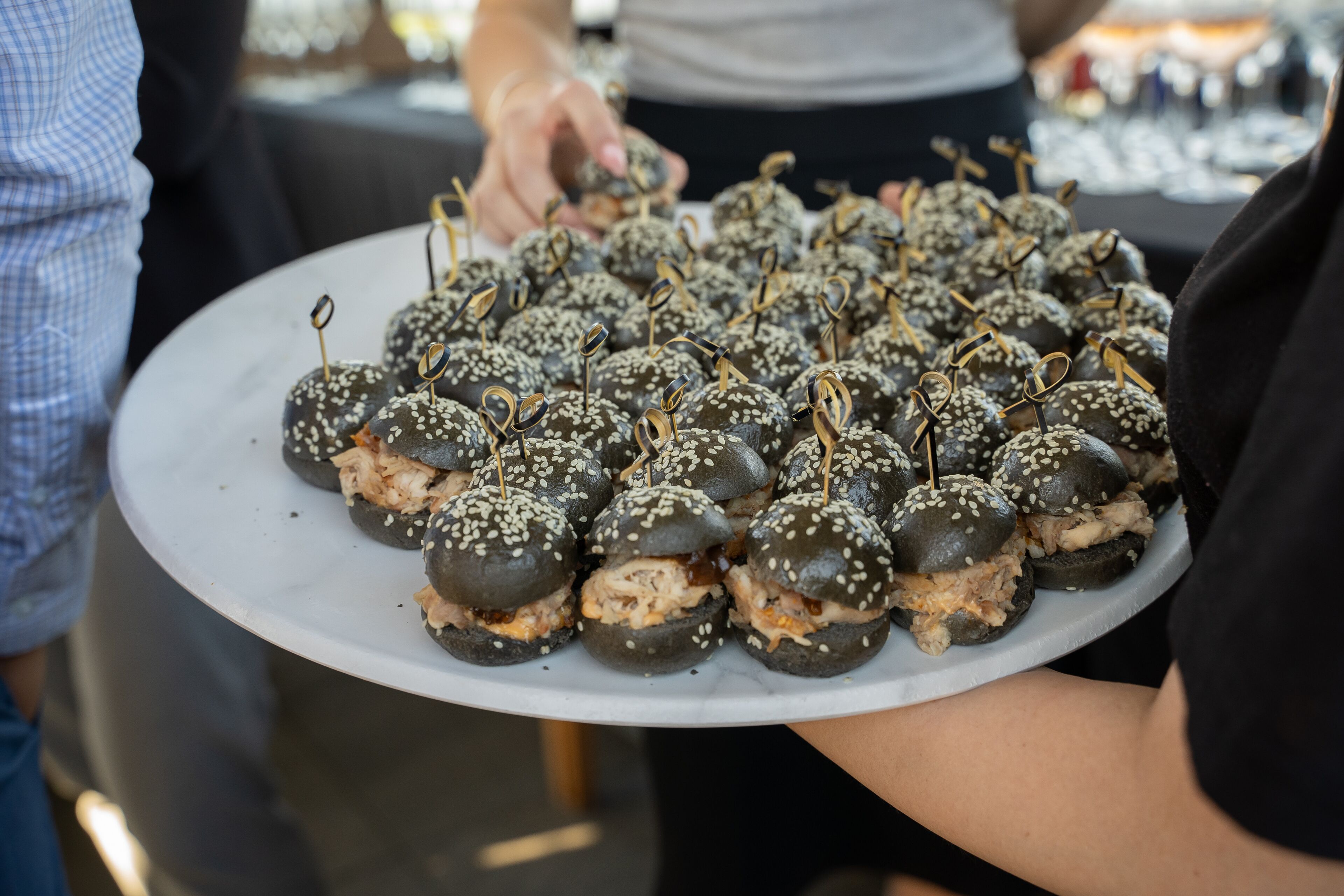 A person holding a tray with round, sesame-seed-covered food items, likely appetizers, at an event.