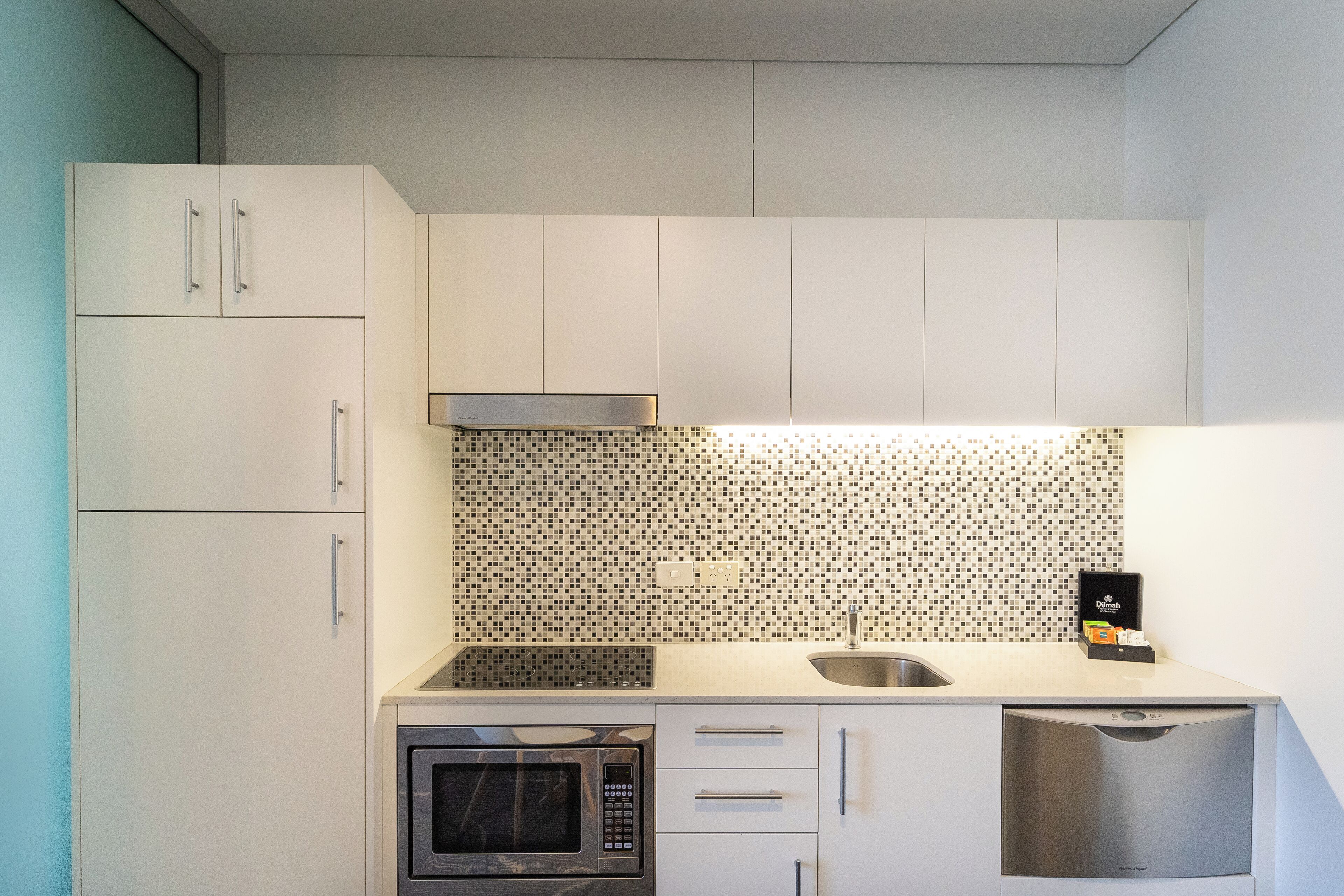 A compact kitchen with white cabinets, a tiled backsplash, a microwave, a dishwasher, and a sink.