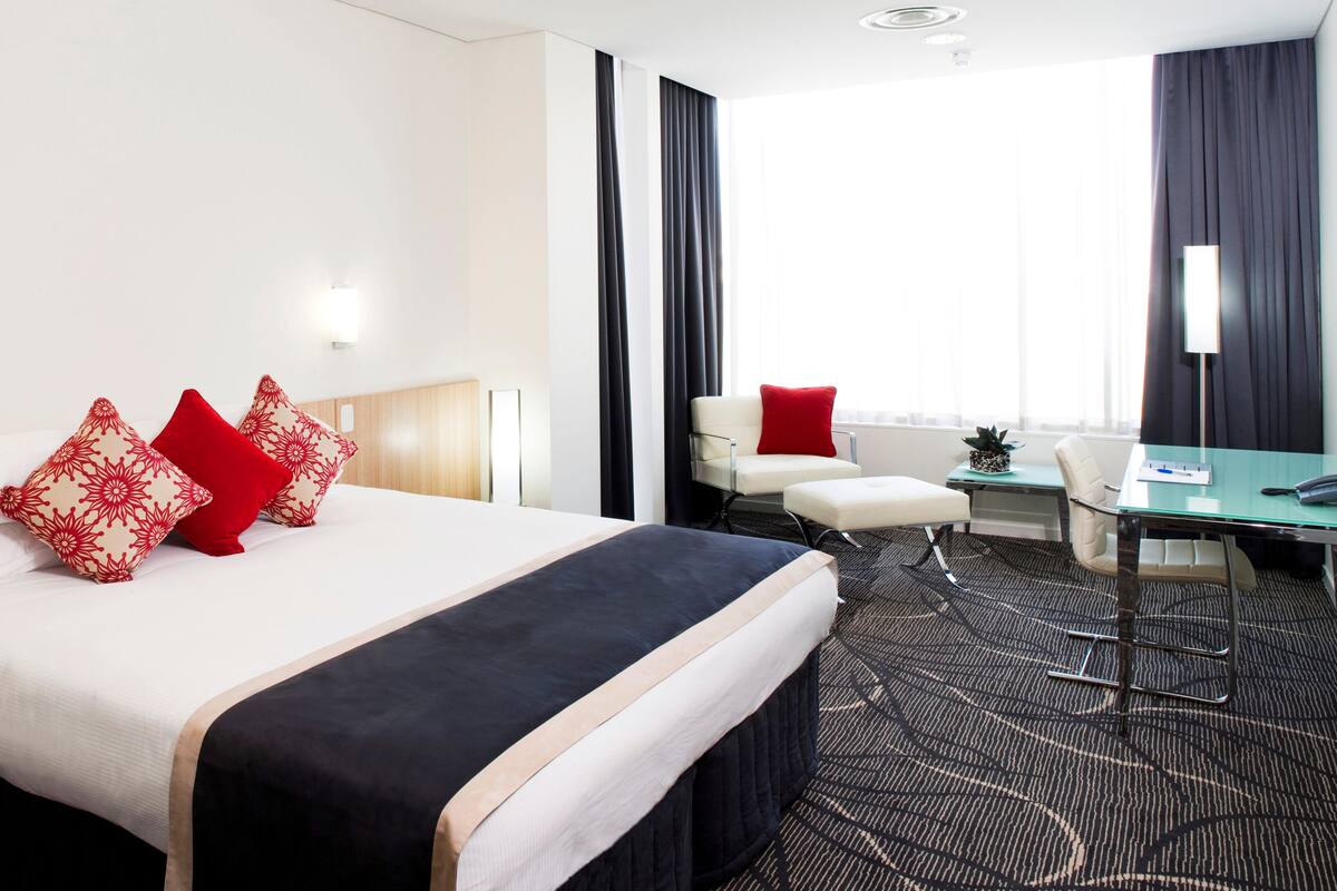 Et hotelværelse med en seng, et skrivebord, en stol og et lille bord.