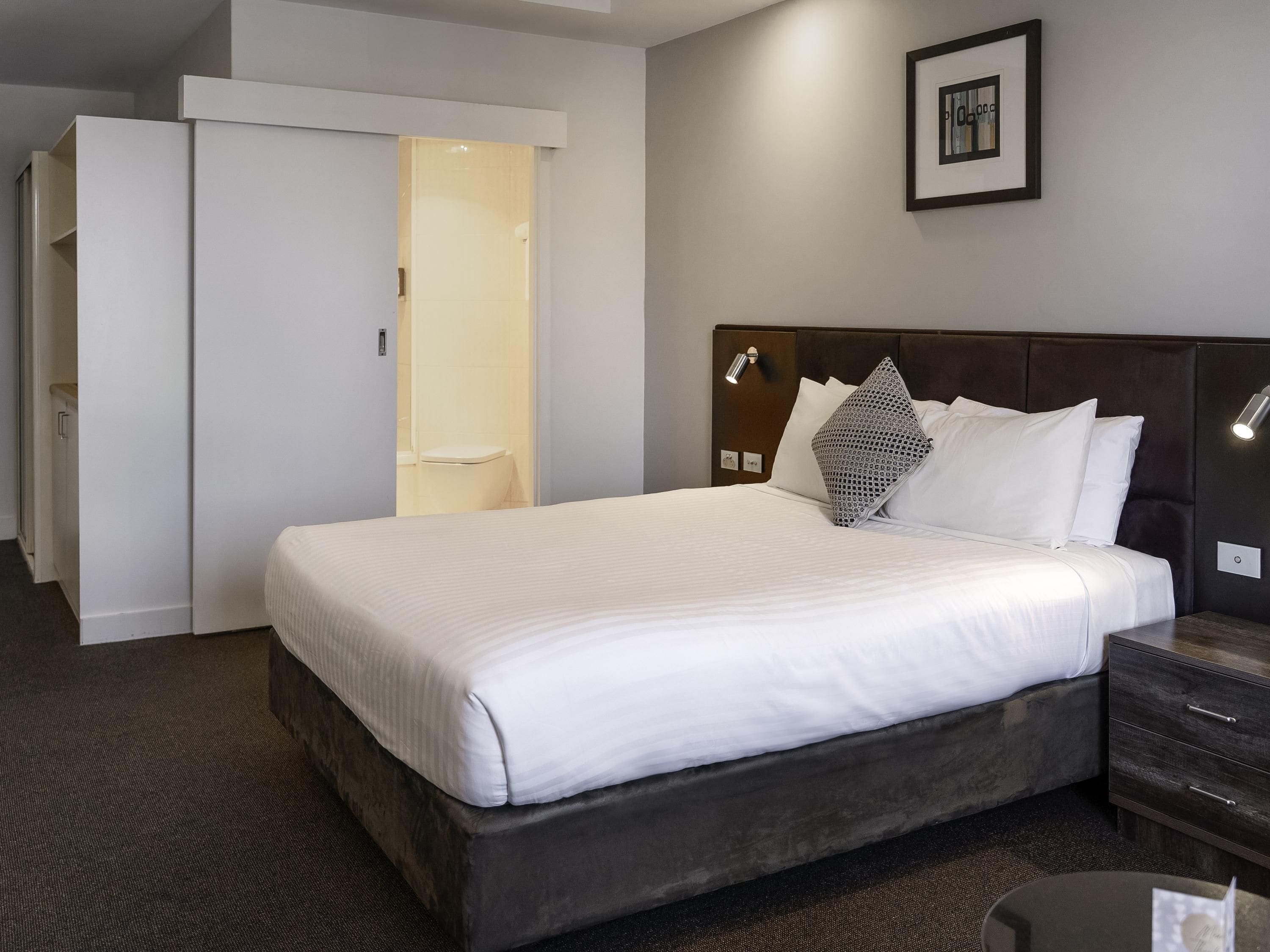 Ein Hotelzimmer mit einem großen Bett, einem Kleiderschrank, einem Nachttisch und einer Wandleuchte.