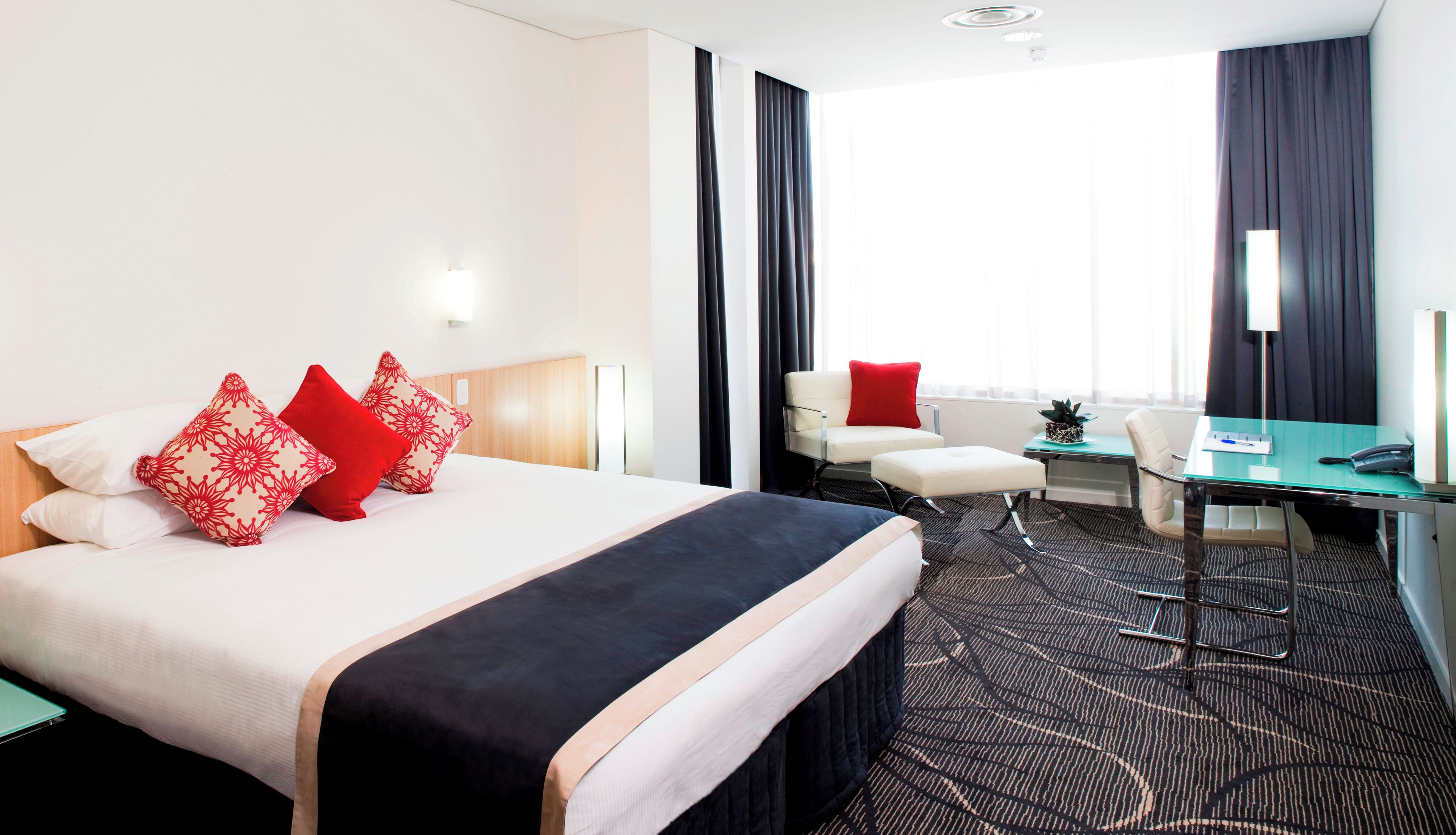 Una habitación de hotel con cama, escritorio, silla y ventana con cortinas.
