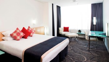 Una habitación de hotel con cama, escritorio, silla y ventana con cortinas.