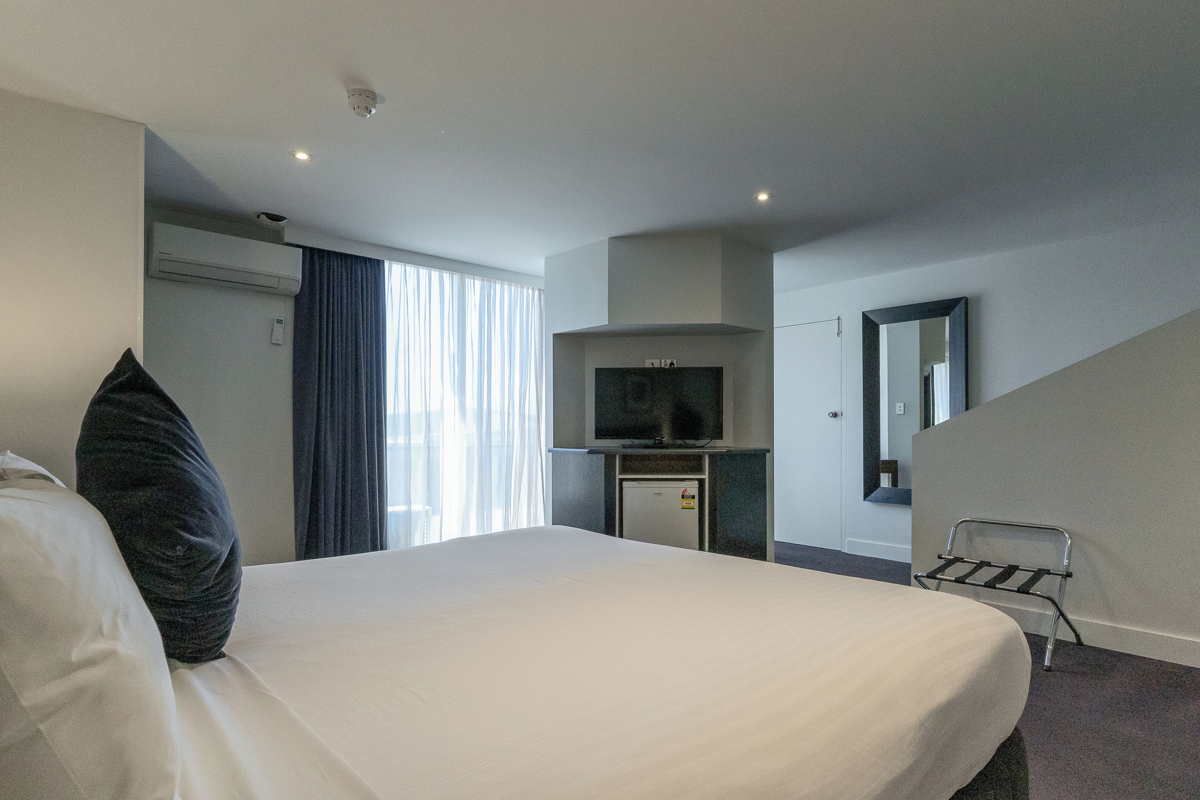 A hotel room with a bed, a TV, a small fridge, and a window with curtains.
