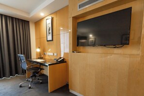 A hotel room with a wooden desk, a chair, a flat-screen TV mounted on the wall, and a telephone.