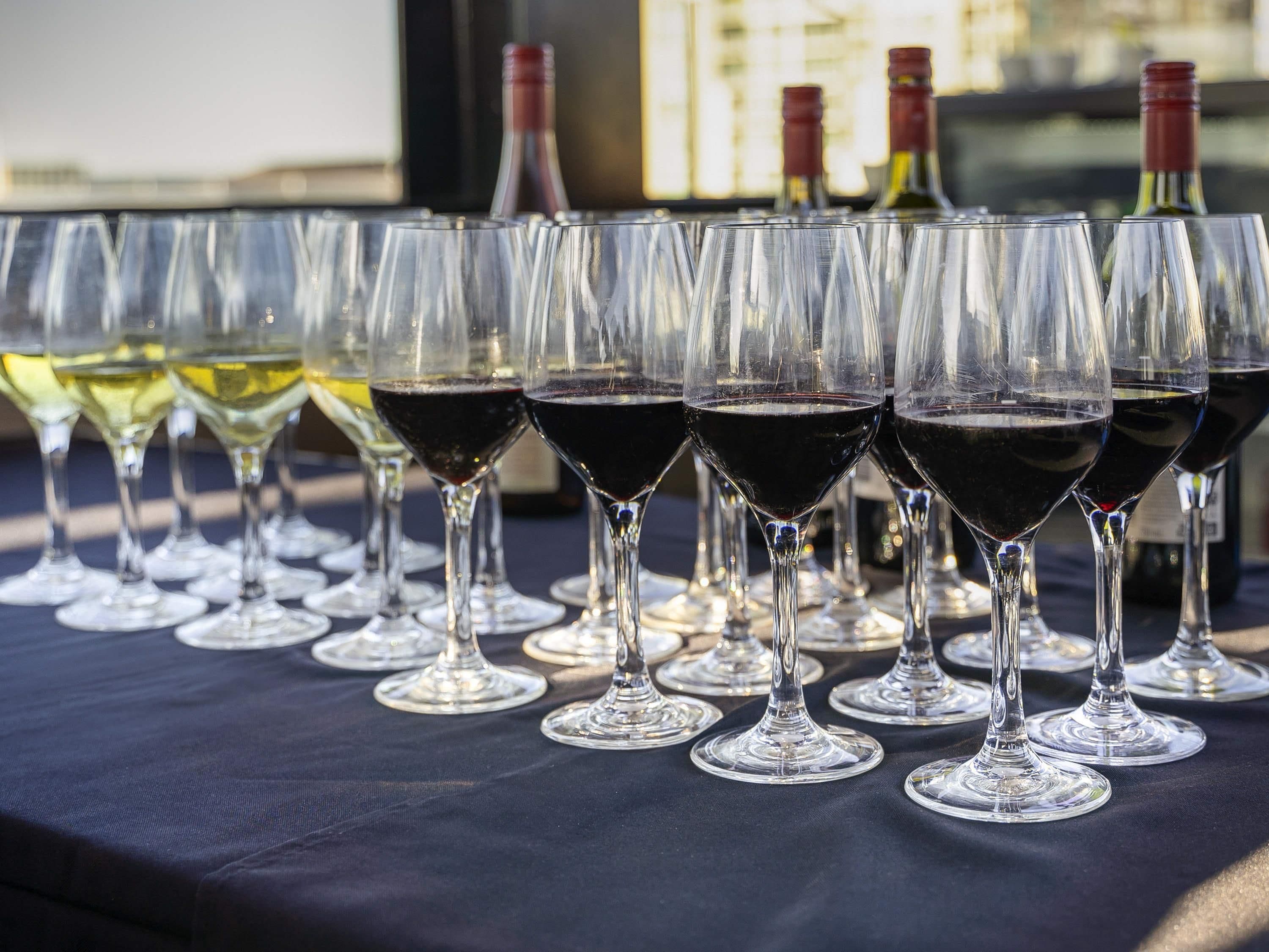 A row of wine glasses on a table with bottles in the background.