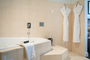 A modern bathroom with a freestanding bathtub, a towel, and two white robes hanging on the wall.