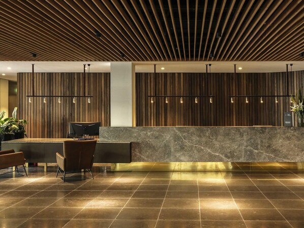 Un área de recepción con techo de listones de madera, mostrador de mármol y una zona de estar con sillones.