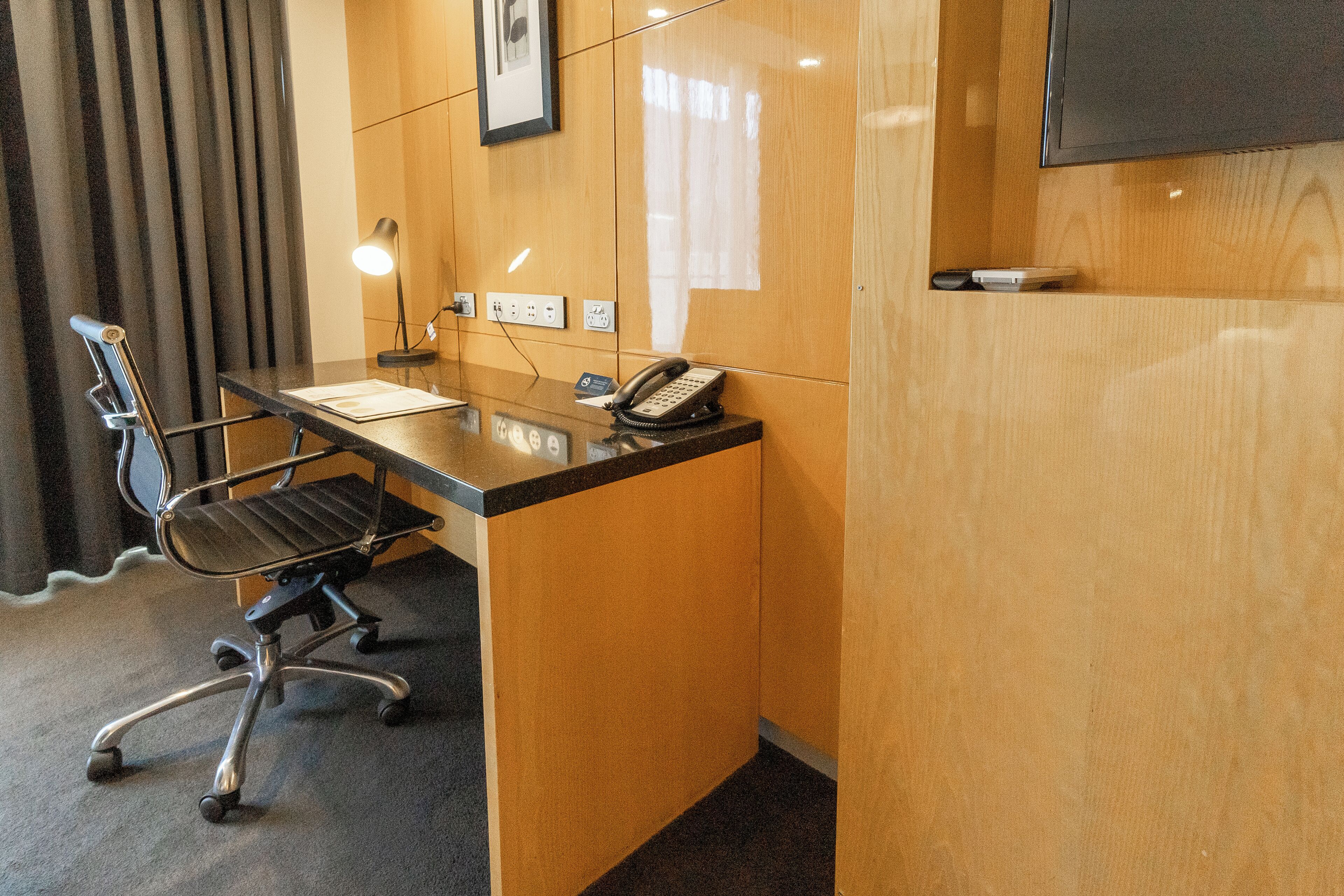 A small office space with a desk, chair, telephone, and a mounted television.