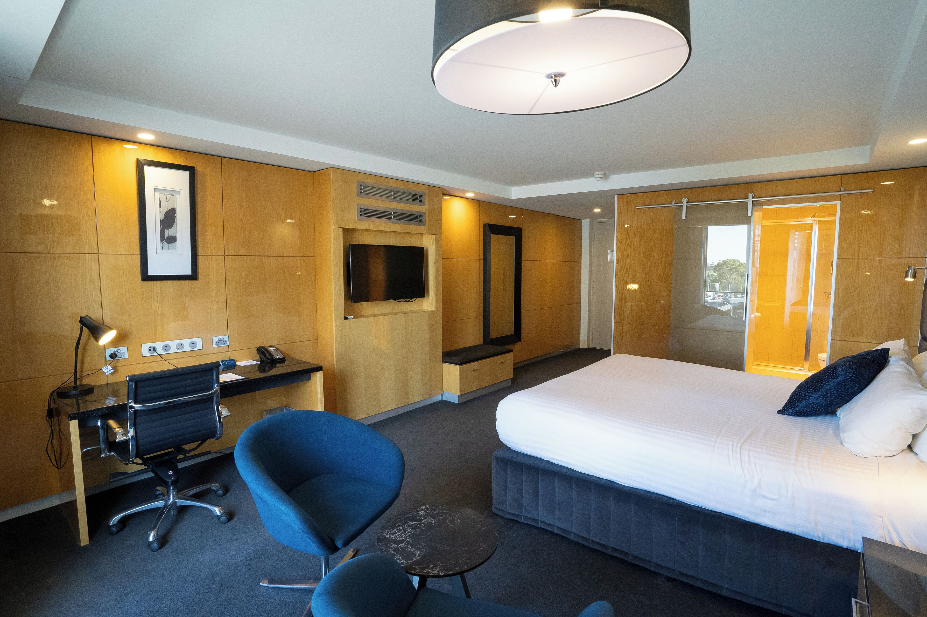 A modern hotel room with a large bed, a desk with a computer, a chair, and a small table.