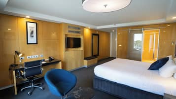 A modern hotel room with a large bed, a desk with a computer, a chair, and a small table.