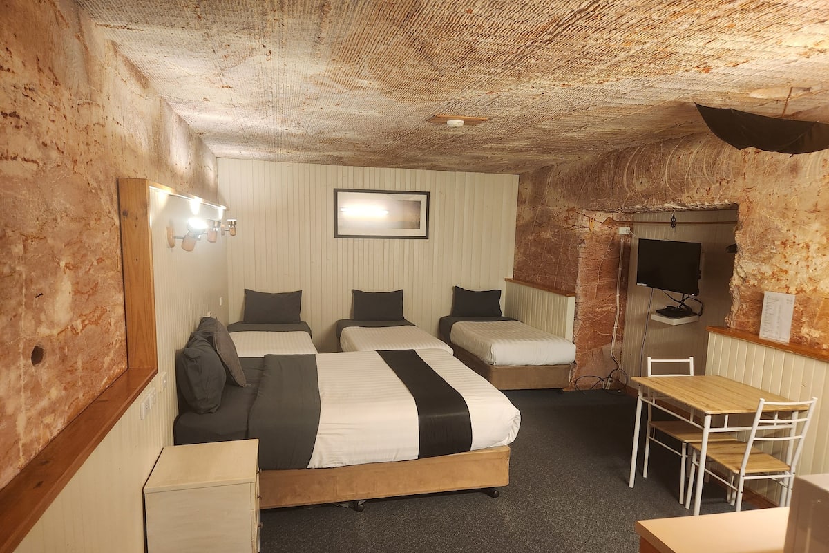 A hotel room with three beds, a desk, a chair, a TV, and a mirror.