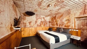 Een eenvoudige kamer met een houten stapelbed, een klein nachtkastje en een televisie aan de muur.