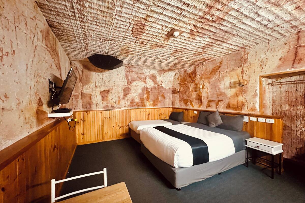 A rustic room with a wooden bunk bed, a small bedside table, and a mounted television.