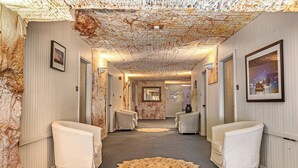 Een hal met een gestructureerd plafond, twee witte fauteuils, een groot rond tapijt en ingelijste foto's aan de wanden.
