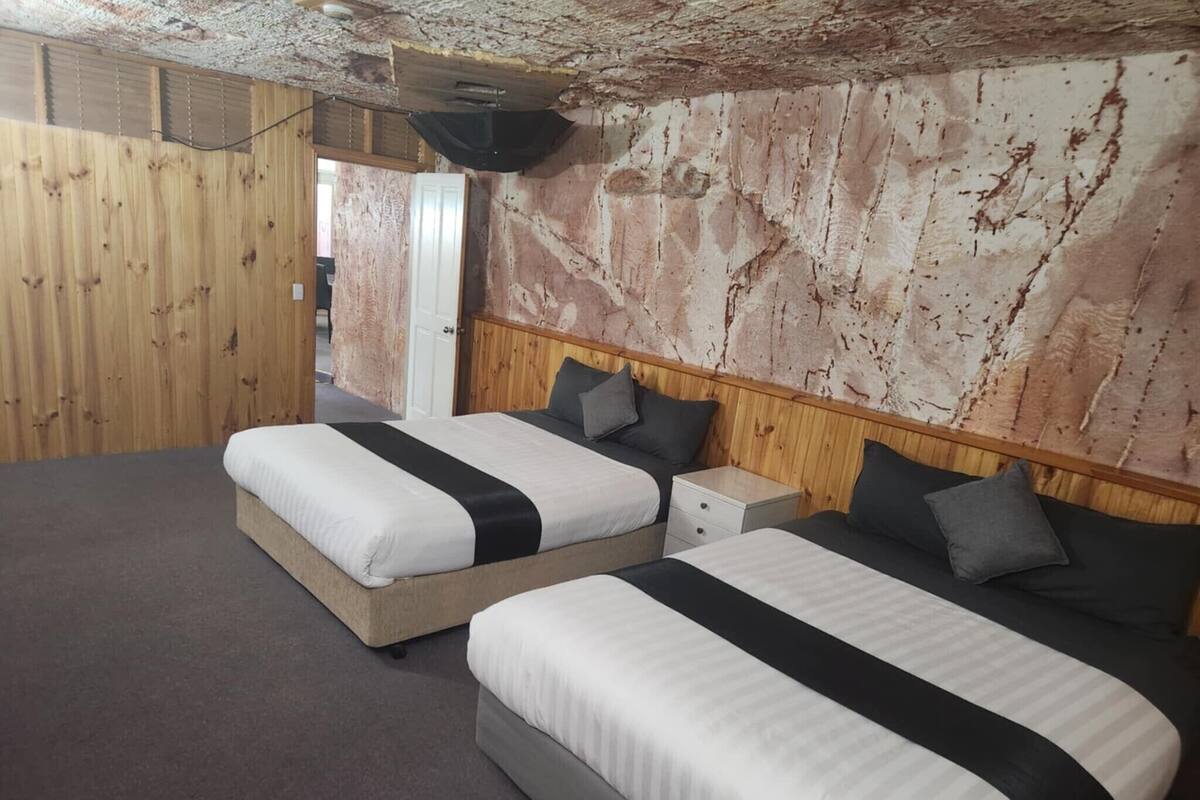 A room with two beds, each with a wooden headboard and a small bedside table.
