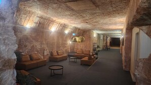 Een ruime lobby met een hoog, gestructureerd plafond en stenen muren, met lederen banken, een bijzettafeltje en een receptiebalie.