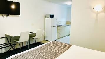 A hotel room with a bed, a desk with chairs, a television, a refrigerator, and a kitchenette.