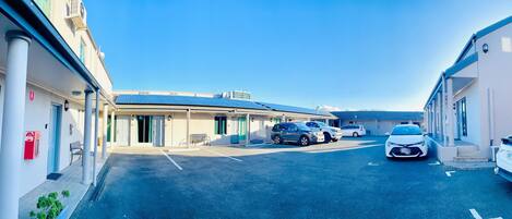 A parking area with several cars, a building with a flat roof, and a clear blue sky.