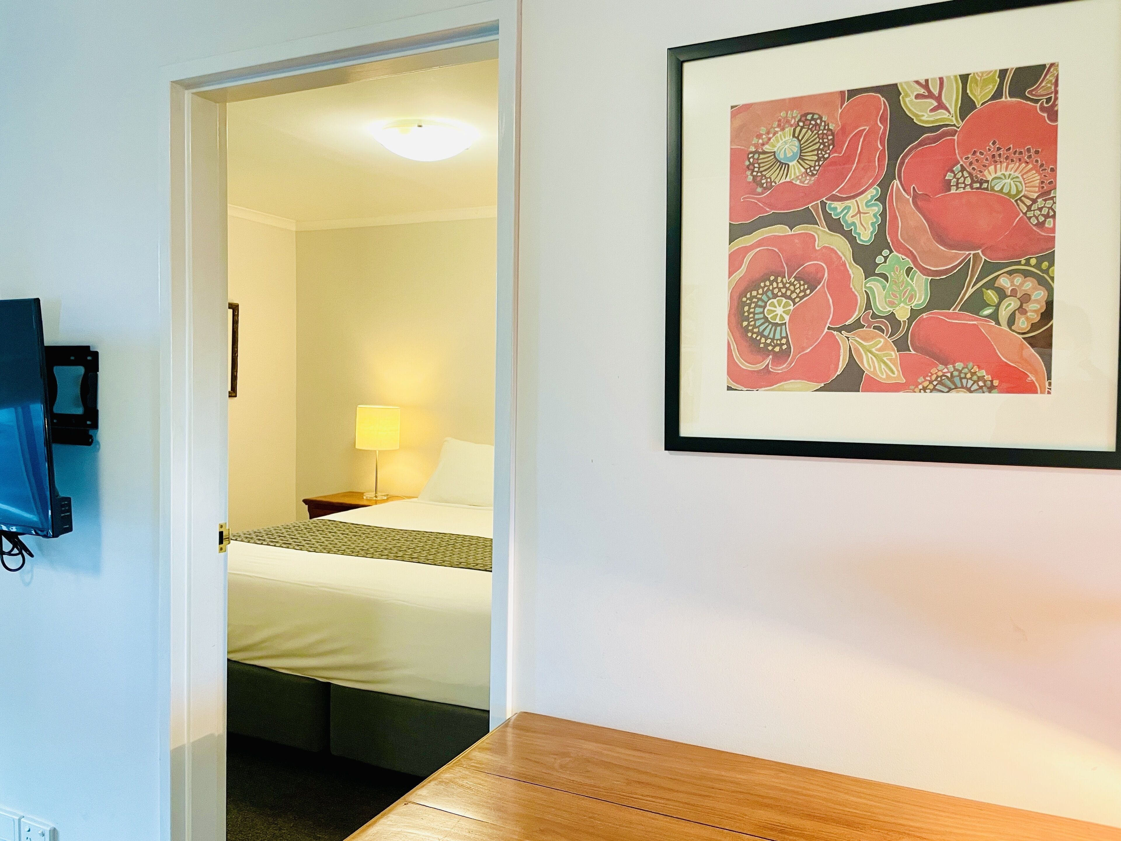 A hotel room with a bed, bedside lamp, and a framed floral artwork on the wall.