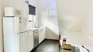 A compact kitchen with a refrigerator, microwave, sink, and dishwasher. There is a small stool and a window with a view of the outside. - The Menzies Ballarat (Bakery Hill)