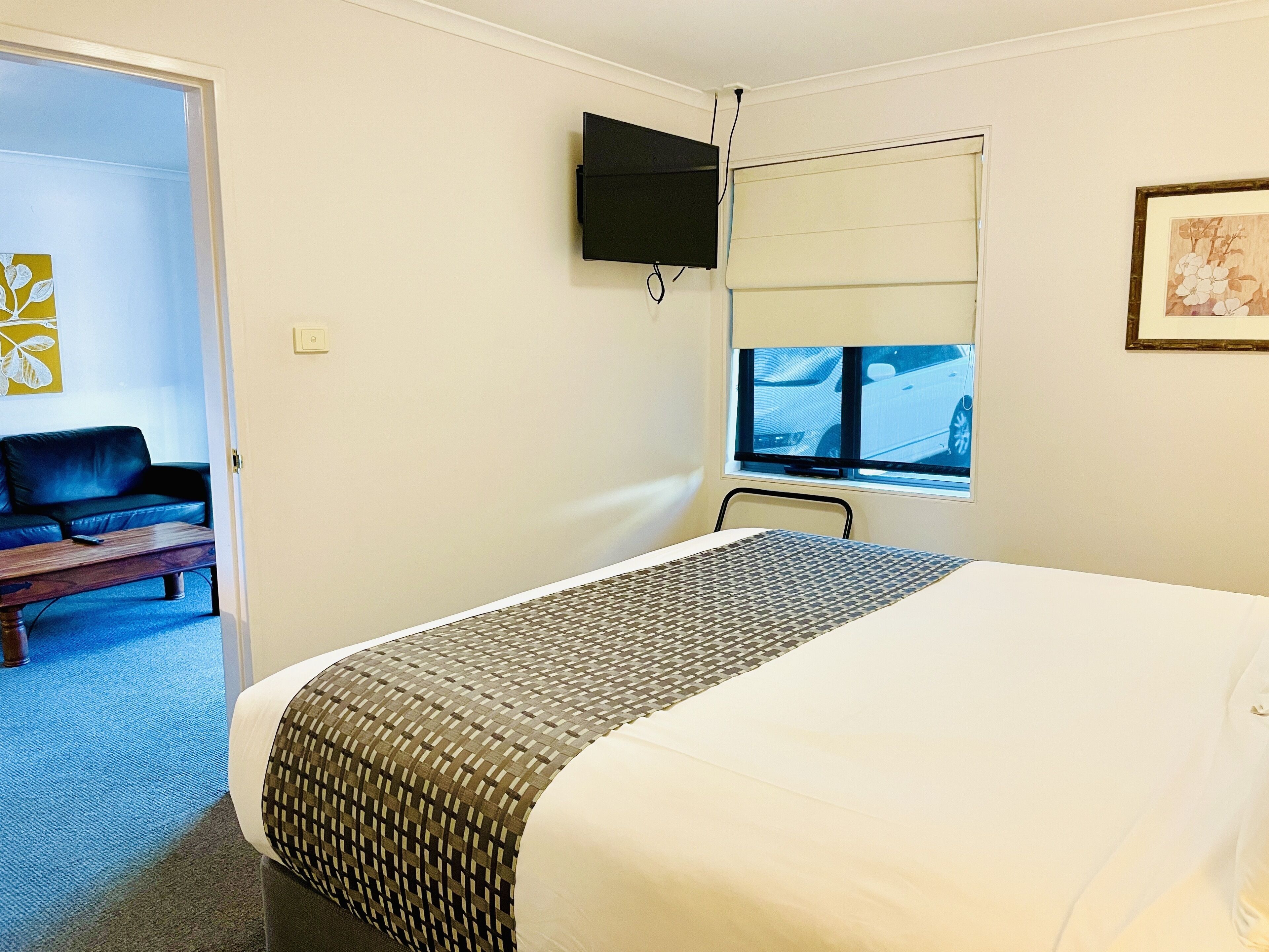 Une chambre d’hôtel avec un lit, un téléviseur fixé au mur, une fenêtre donnant sur un paysage agréable, un canapé et un tableau au mur.