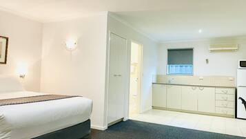 A hotel room with a bed, a small kitchenette, and a bathroom visible through an open door.