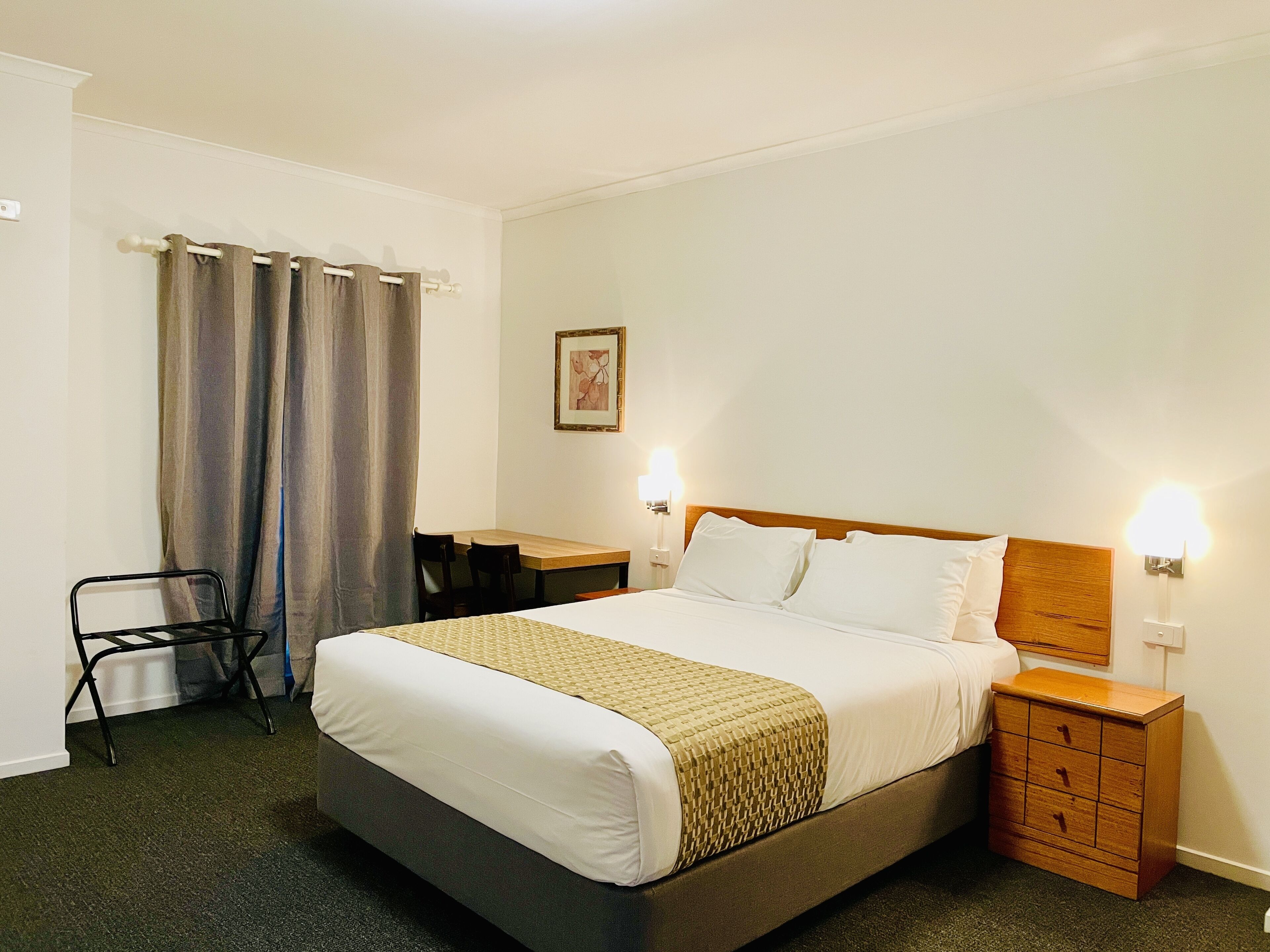 Una habitación de hotel con cama, mesitas de noche, escritorio, silla y cortinas.
