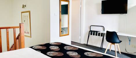 A hotel room with a bed, a desk with a chair, a television, and a door leading to another room.