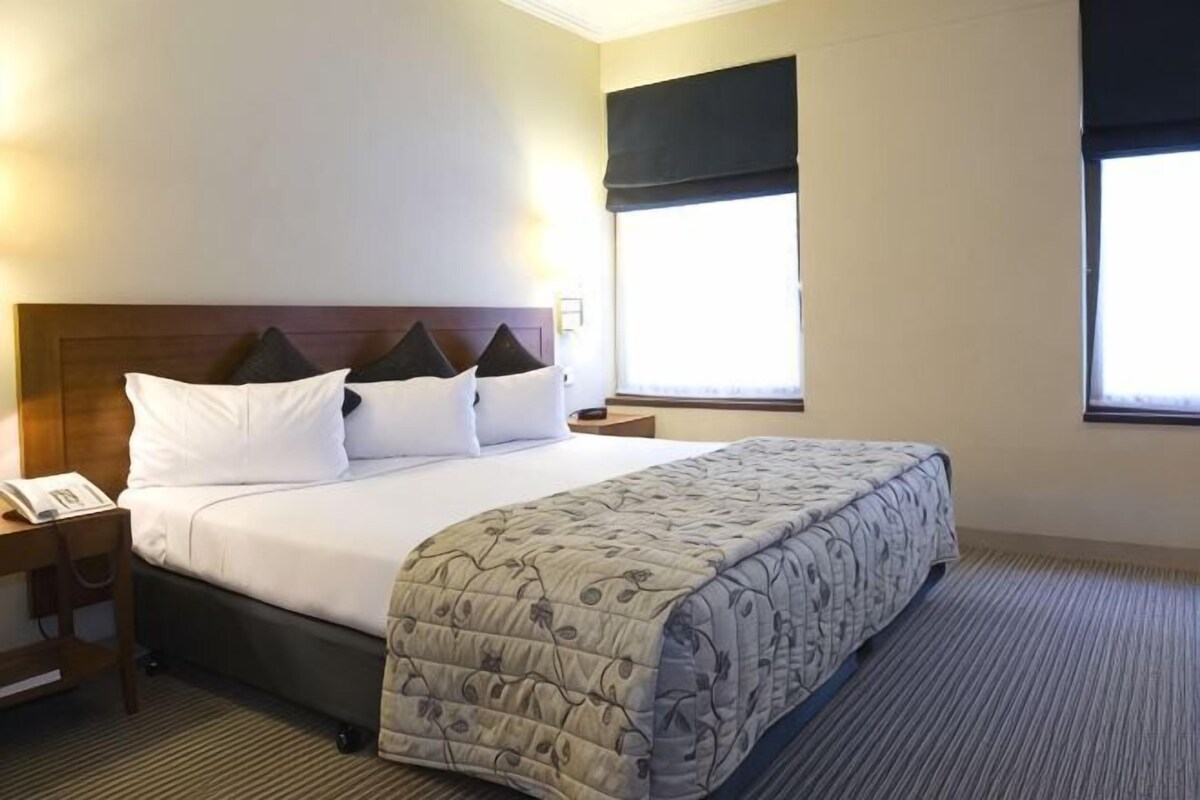 A hotel room with a bed, a bedside table, a telephone, and a window.