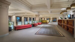 A spacious lobby with a central red seating area, a reception desk, and a patterned carpet. - Batman’s Hill on Collins (Melbourne)
