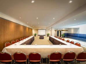 A conference room with a long table, red chairs, a projector screen, and a blue seating area. - Batman’s Hill on Collins (Melbourne)