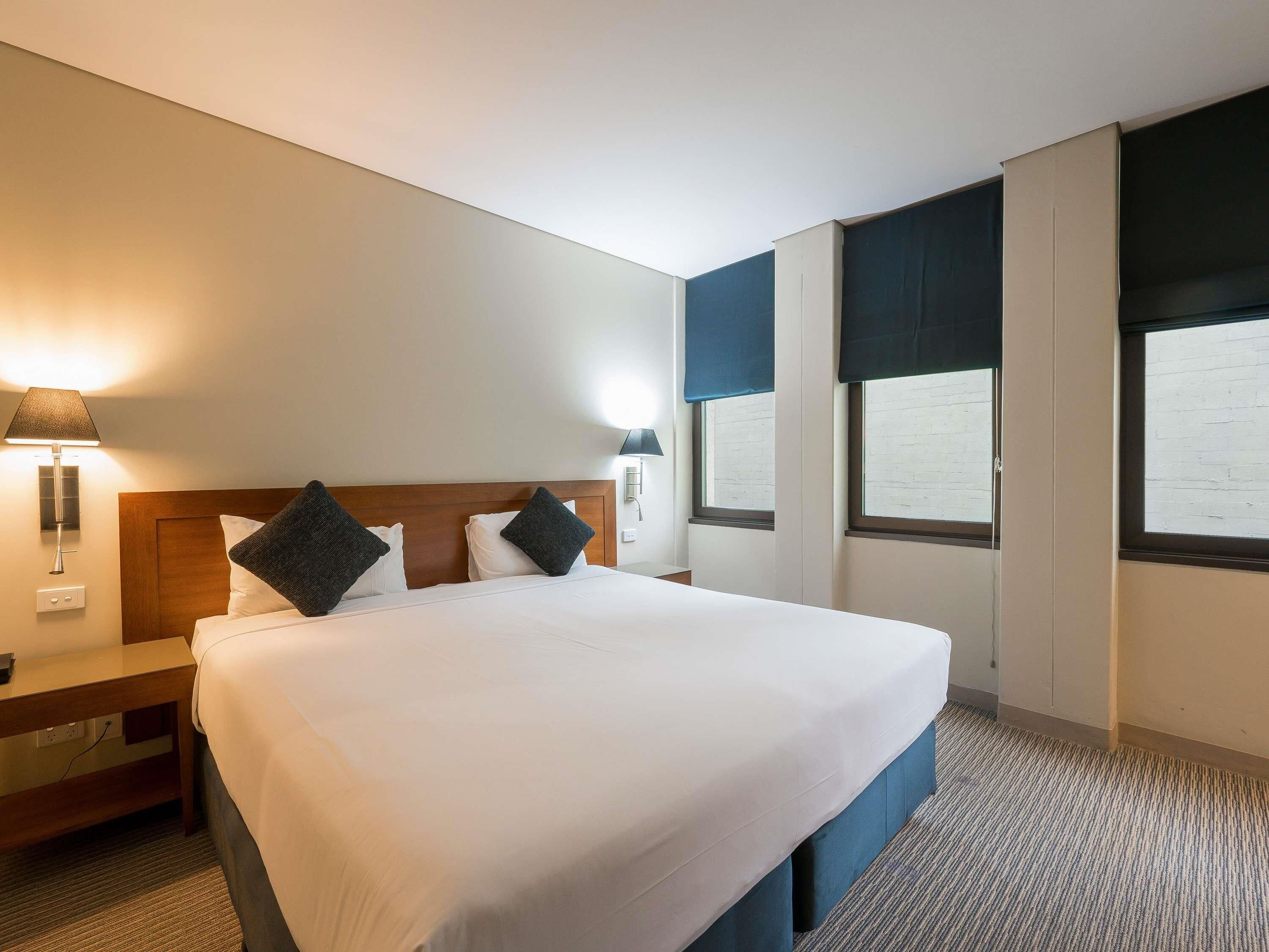 Een hotelkamer met een groot bed, twee nachtkastjes, een muurlamp en een raam met uitzicht.