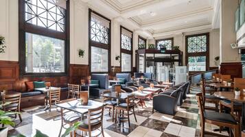 Un restaurante espacioso con techos altos, grandes ventanales y una variedad de opciones de asientos, incluyendo cabinas y mesas.