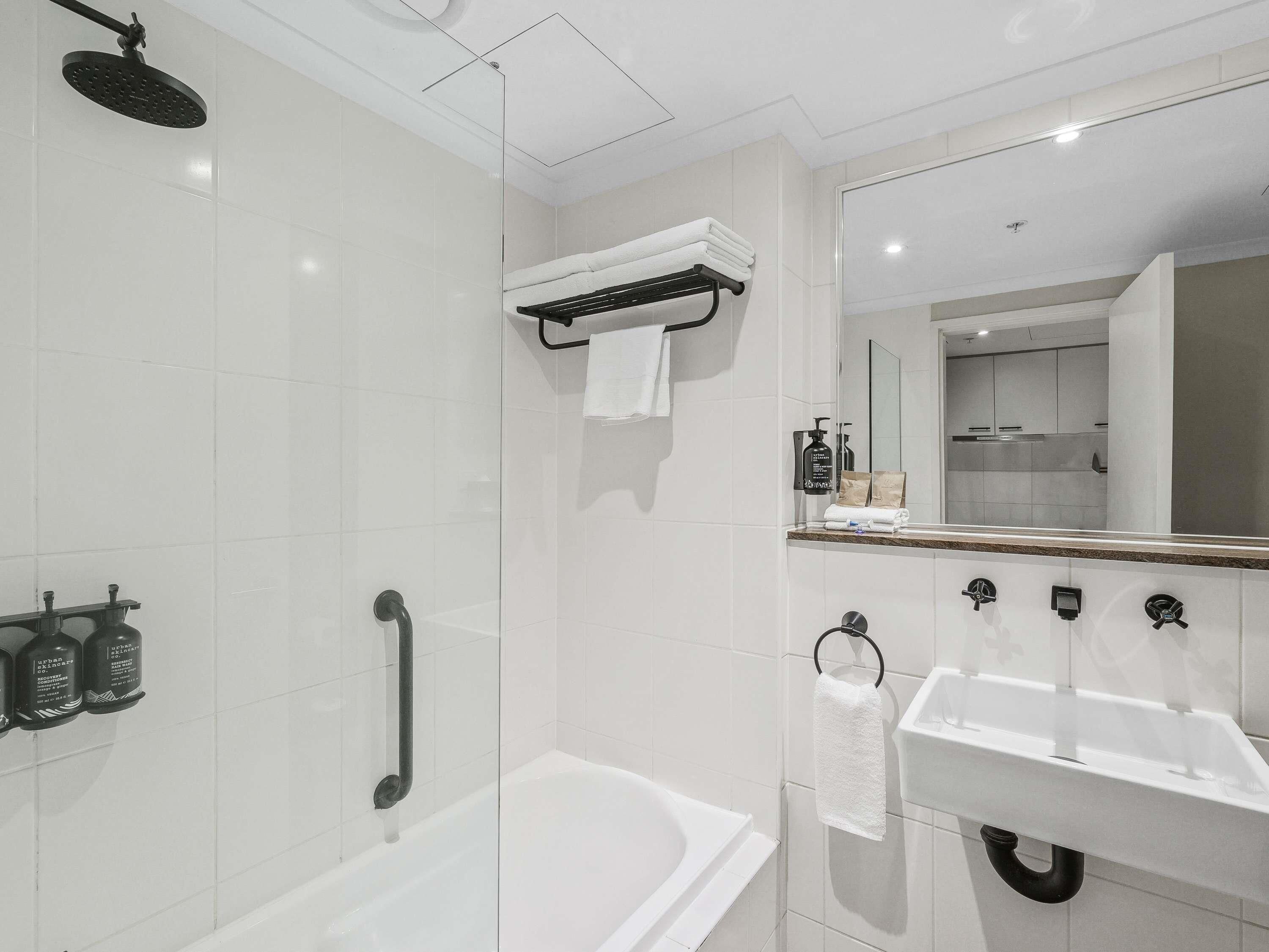 A modern bathroom with a glass-enclosed shower, a white bathtub, a sink with a mirror, and a towel rack.