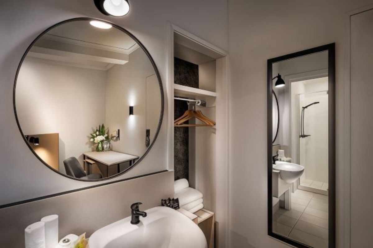 A modern bathroom with a large round mirror, a white sink, and a shower area.