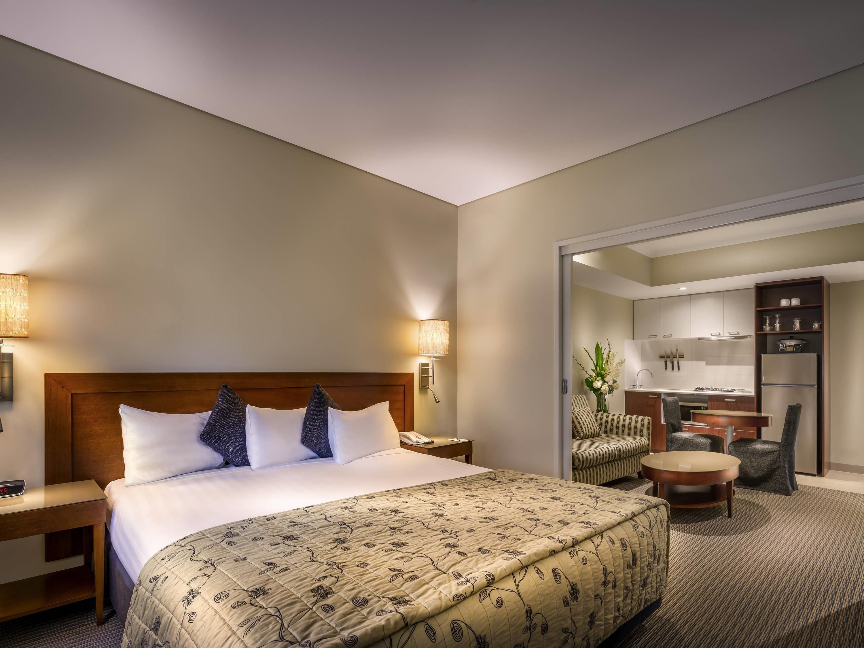 A hotel room with a bed, bedside tables, a desk, a chair, and a kitchenette.