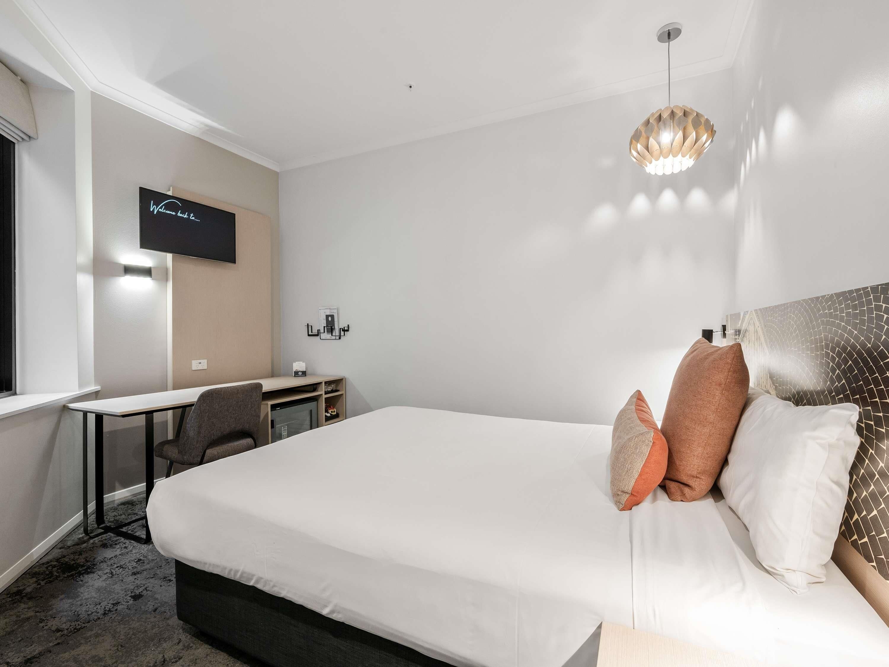Habitación de hotel con cama, escritorio, silla, televisión y una lámpara de techo original.