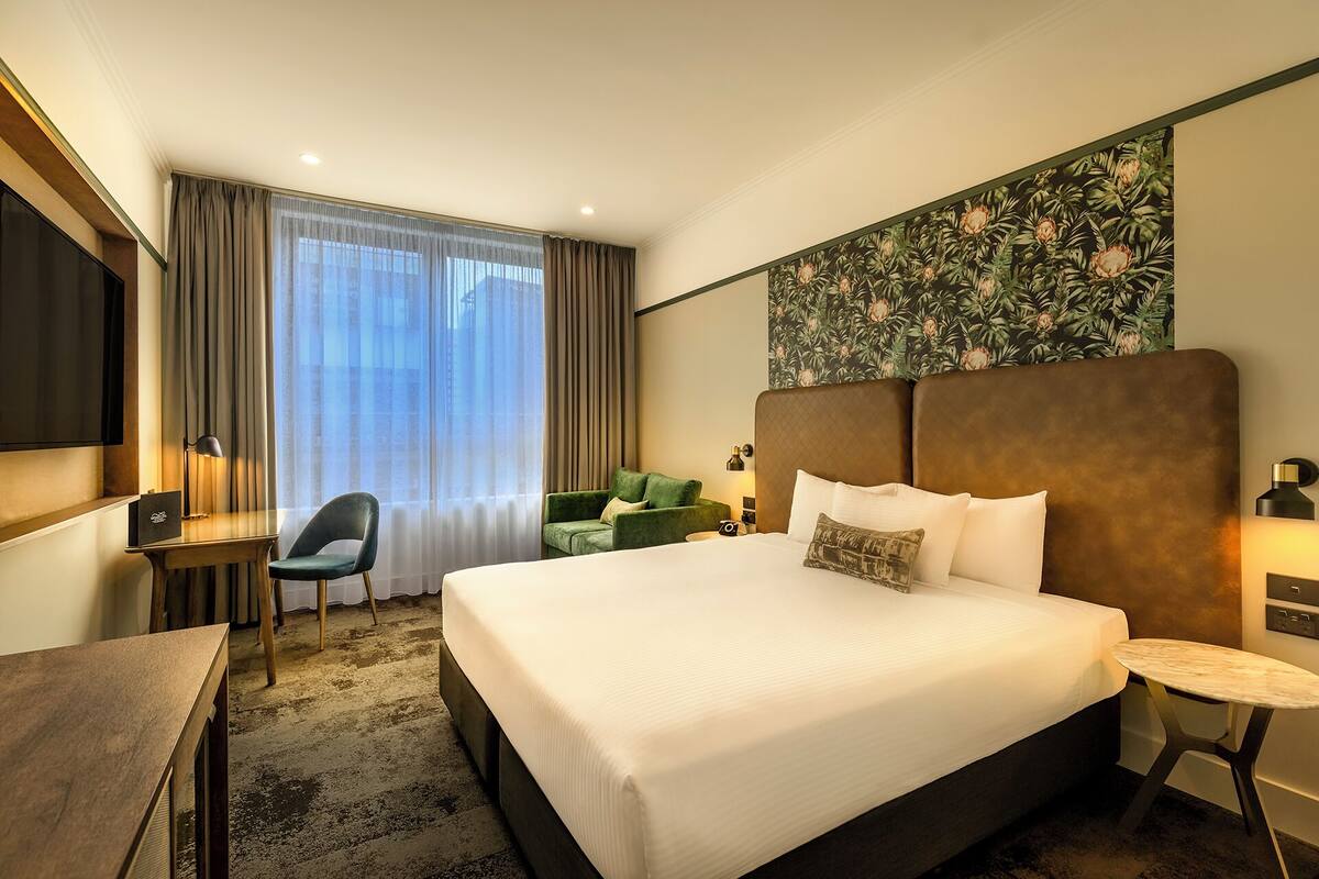 Quarto de hotel com uma cama grande, uma mesa de escritório, uma cadeira, uma mesinha e uma televisão.