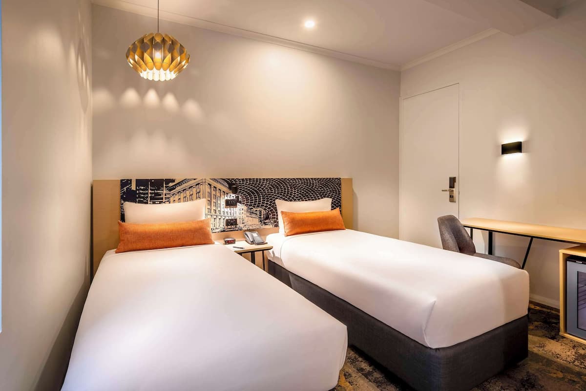 Two single beds with white linens and accent pillows, flanked by nightstands and a unique pendant light.