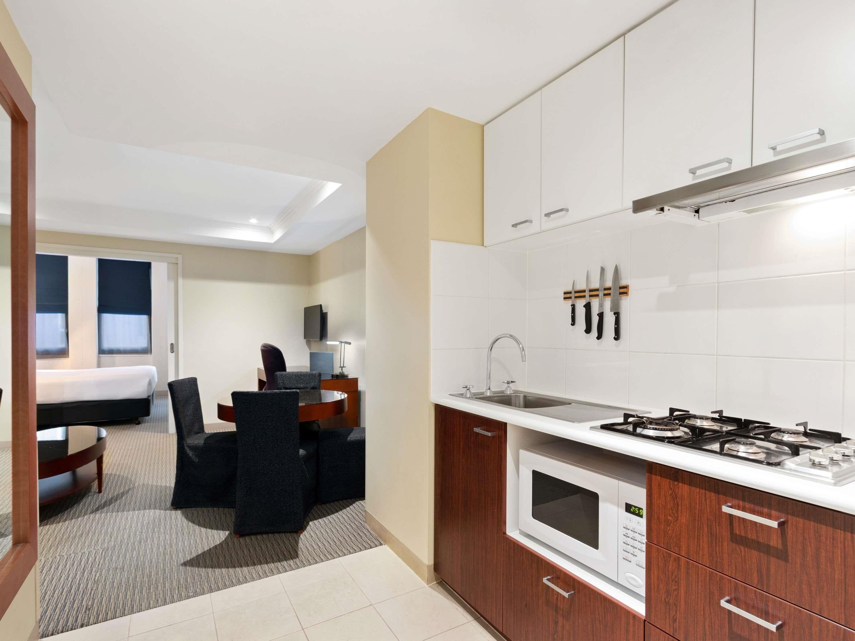 Una habitación de hotel compacta con kitchenette, cama, escritorio y silla.