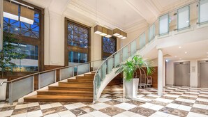 A spacious lobby with a marble floor, a staircase with glass railings, and large windows offering views of the outside. - Batman’s Hill on Collins (Melbourne)