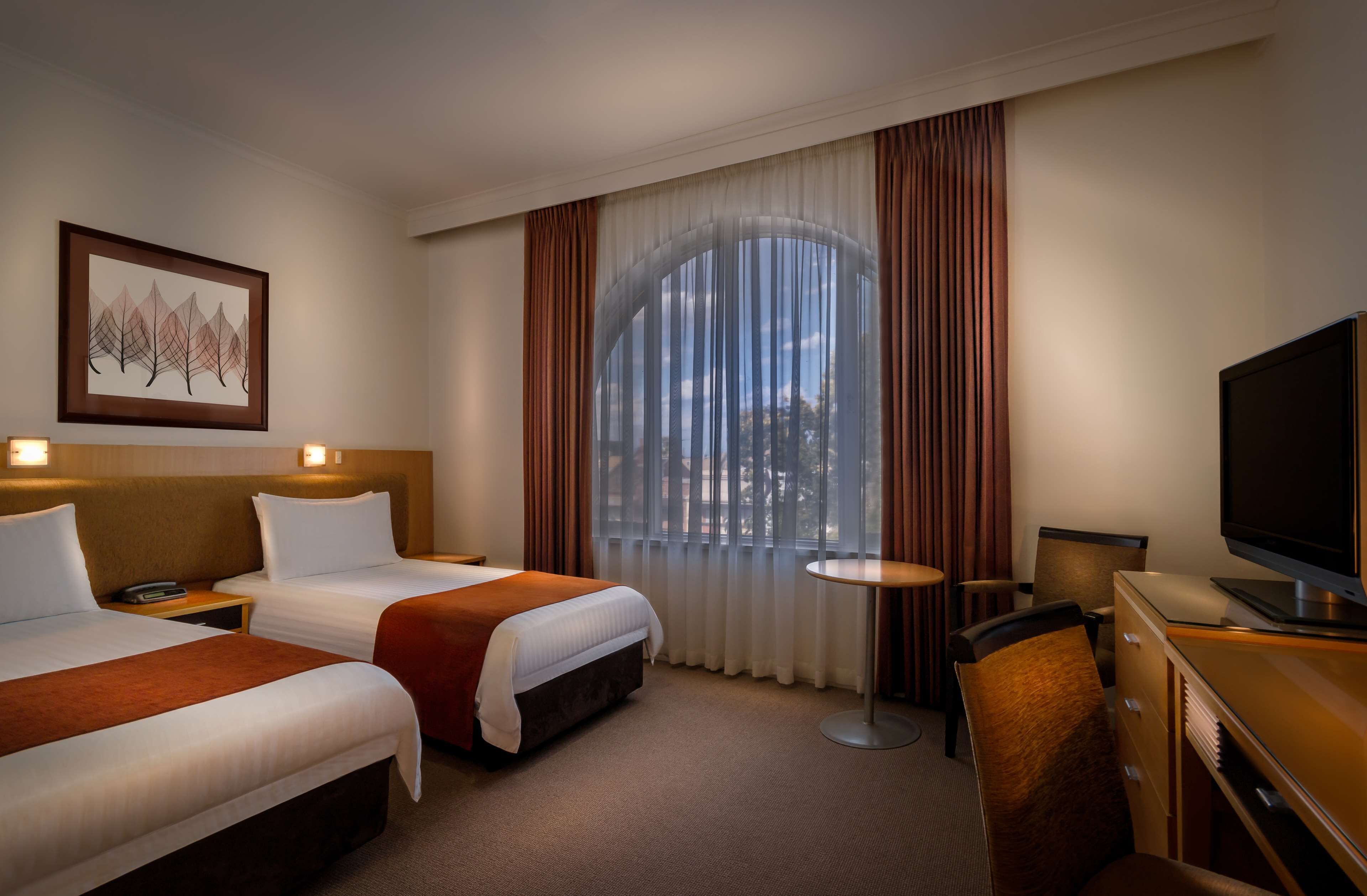A hotel room with two beds, a television, a desk, and a window with curtains.