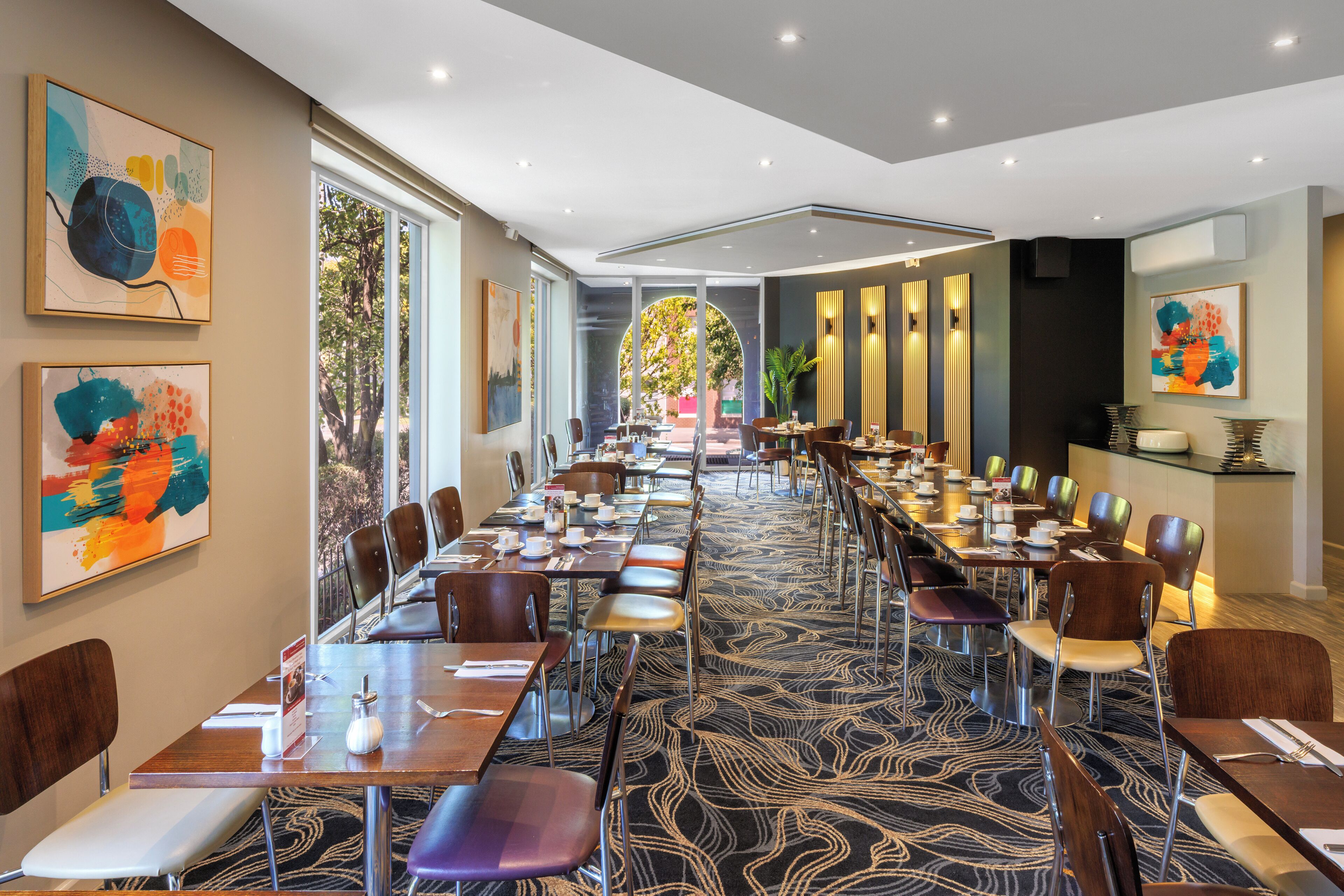 Un comedor de hotel con mesas largas, sillas y obras de arte en las paredes.