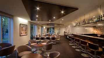 Un comedor moderno con mesas redondas y taburetes de bar, ventanas amplias y una barra con estantes llenos de botellas.