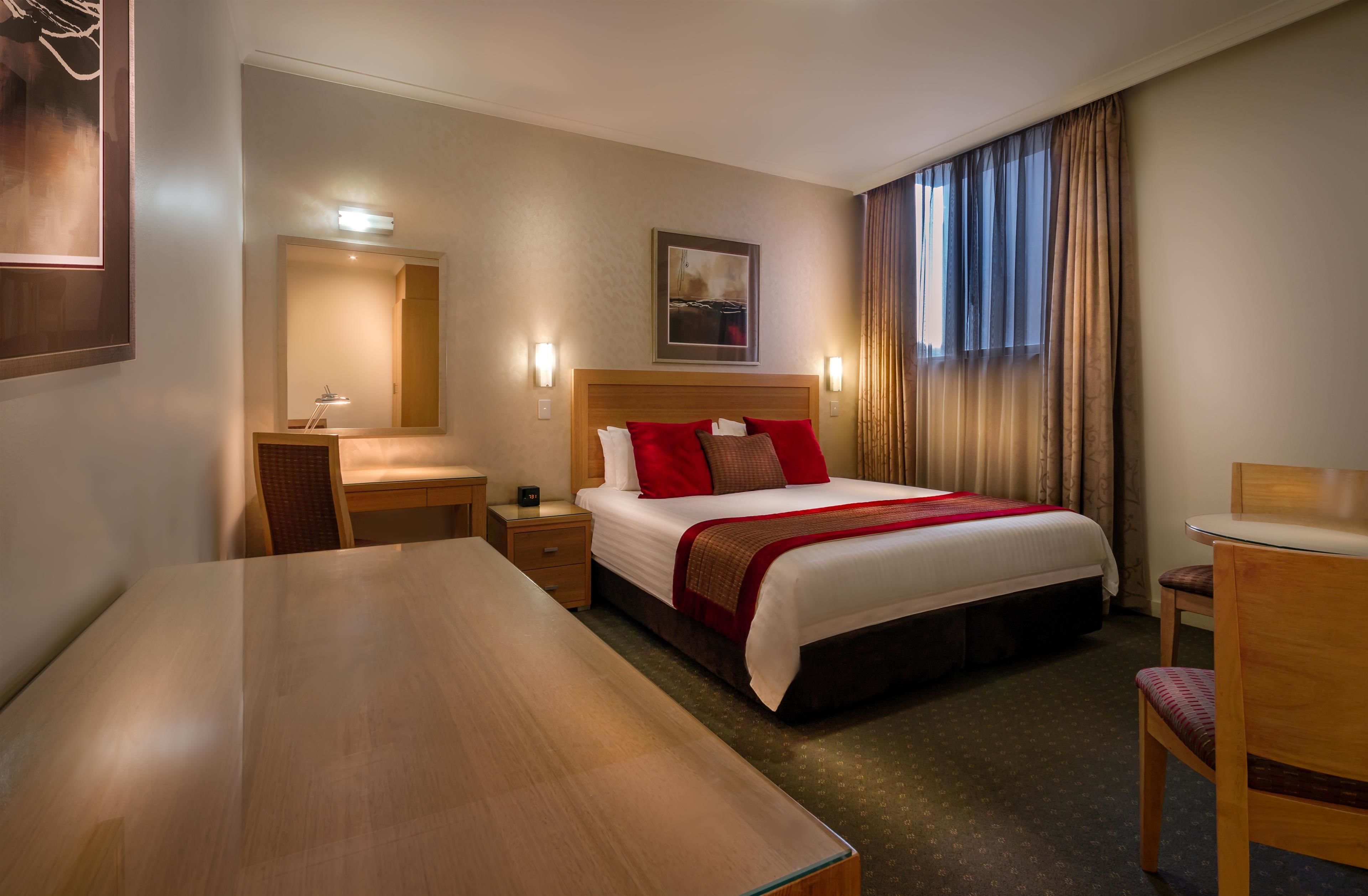 Une chambre d’hôtel avec un grand lit, un bureau, une chaise, une table de chevet, un miroir et une fenêtre avec des rideaux.