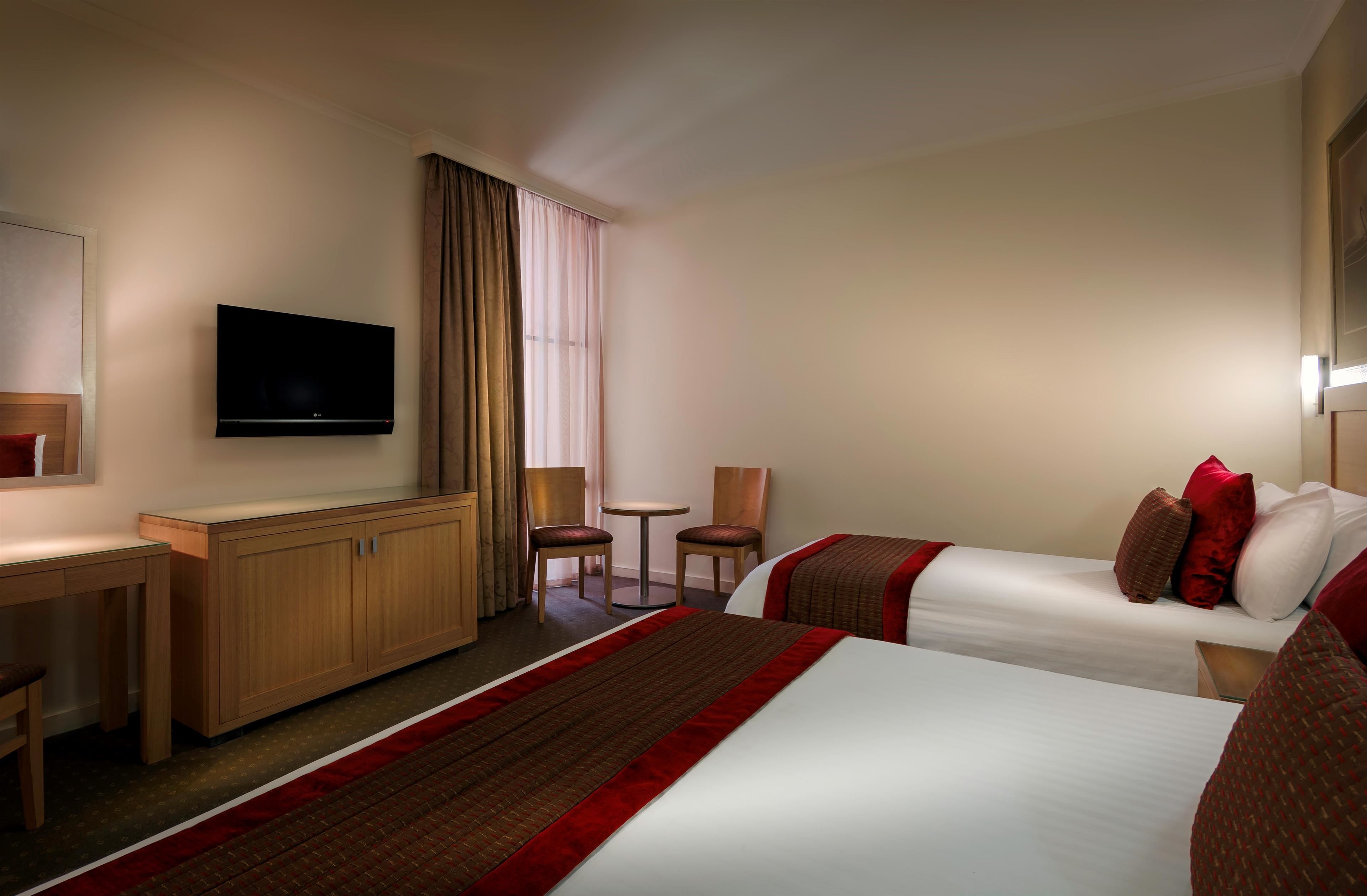 Une chambre d’hôtel avec deux lits, un bureau, une télévision et une petite table.